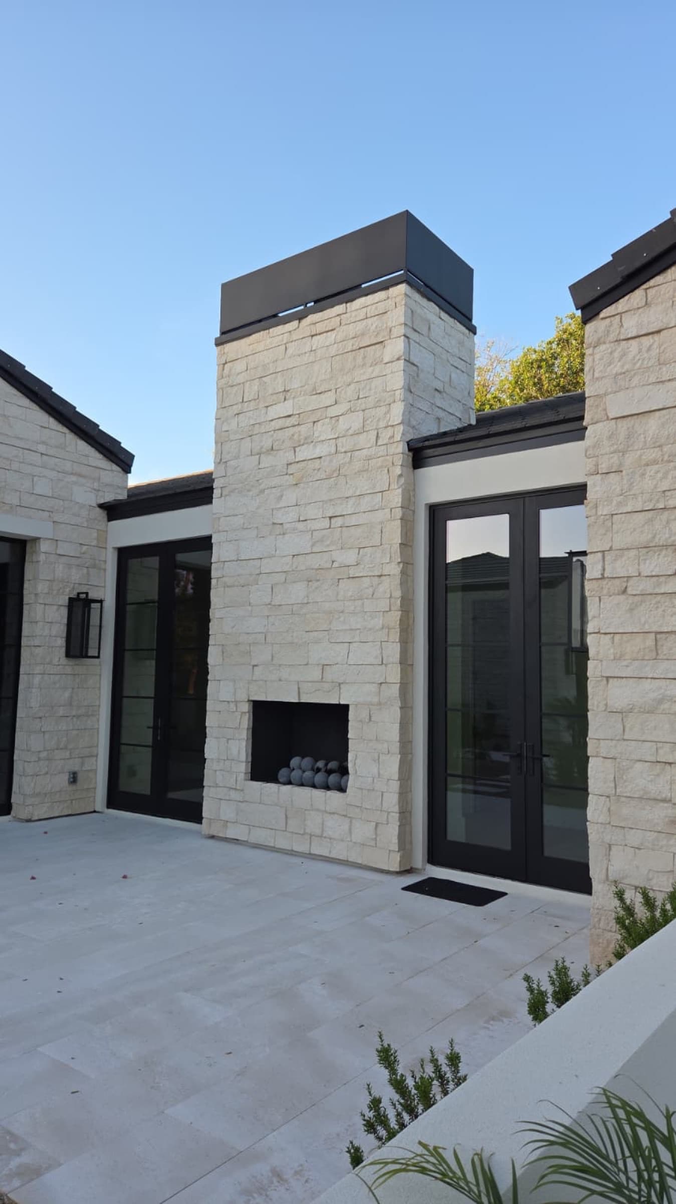 Light stone exterior fireplace with black-framed doors